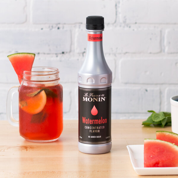 A close-up of a Monin Watermelon Concentrated Flavor bottle next to a slice of watermelon.