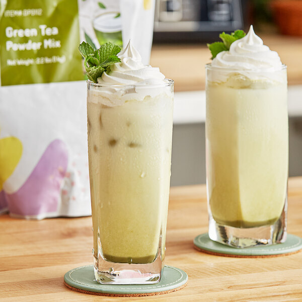 A close up of a glass of green liquid with a white straw and whipped cream and mint leaves.