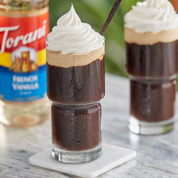 A glass of brown liquid with whipped cream on top.