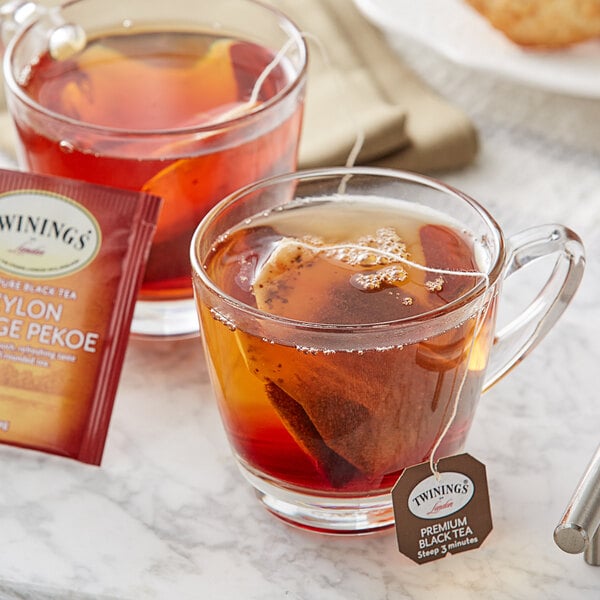 A glass cup of Twinings Ceylon Pure Black Tea with a tea bag in it.