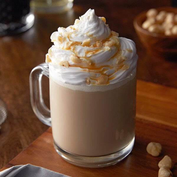 A glass mug of coffee with whipped cream and Monin Hazelnut Syrup with nuts on top.