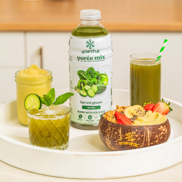 A glass of green Smartfruit Harvest Greens juice with cucumber and mint on a tray.