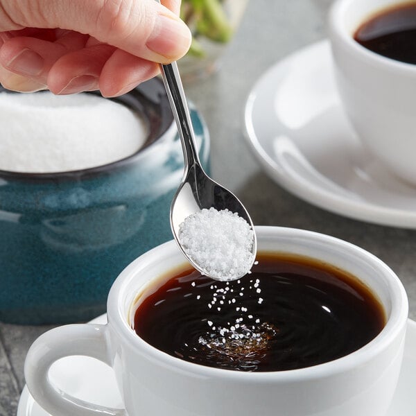 A hand holding a spoon with Splenda Monk Fruit sweetener in a cup of coffee.