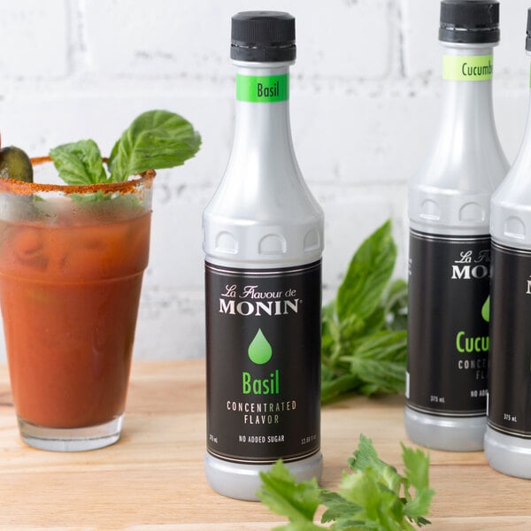 A white Monin bottle with black and green text next to a glass of liquid.