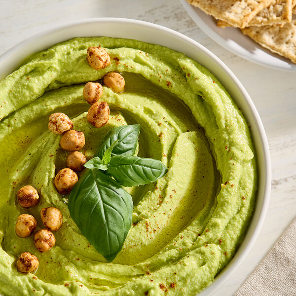 A bowl of hummus with basil and chickpeas on a white background.