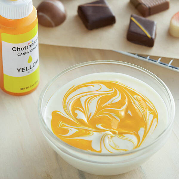 A bowl of white liquid with yellow swirls in it next to a bottle of Chefmaster Yellow Oil-Based Candy Color.