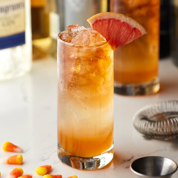 A glass of orange drink with Monin candy corn syrup and ice, garnished with a grapefruit slice.