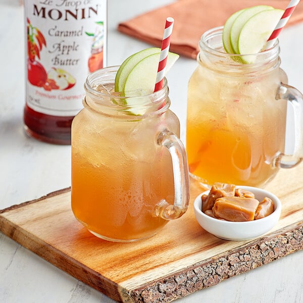 A couple of glasses of caramel apple drinks with straws and apple slices.