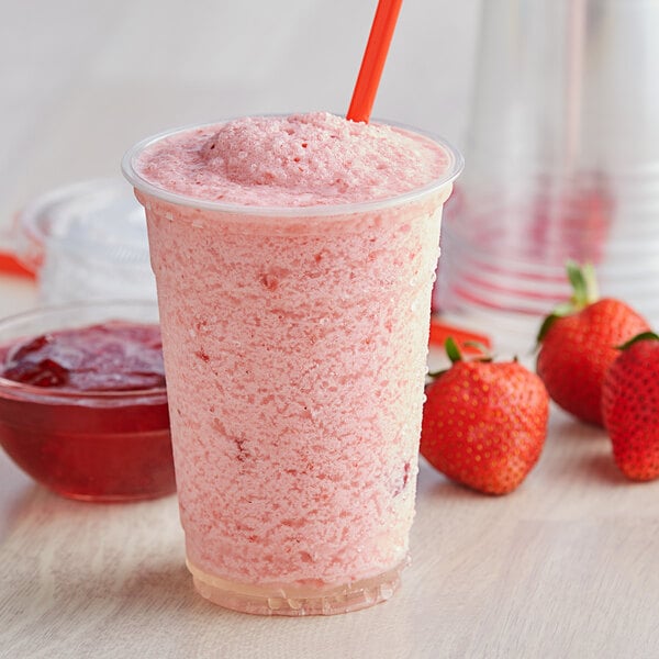 A plastic cup of red strawberry smoothie with a straw in it.