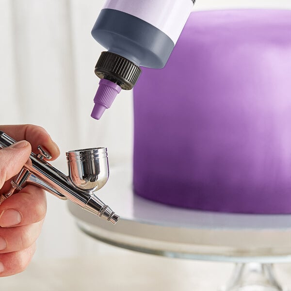 A person using Chefmaster Neon Brite Purple airbrush color to decorate a purple cake.