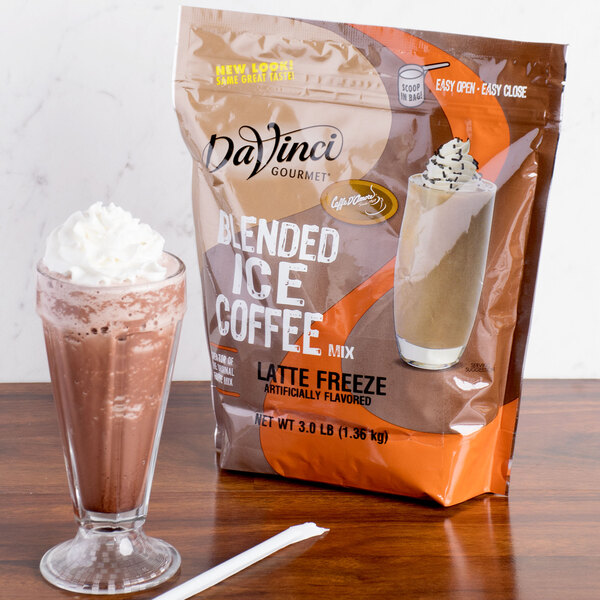 A glass of latte next to a bag of DaVinci Gourmet Latte Freeze mix.