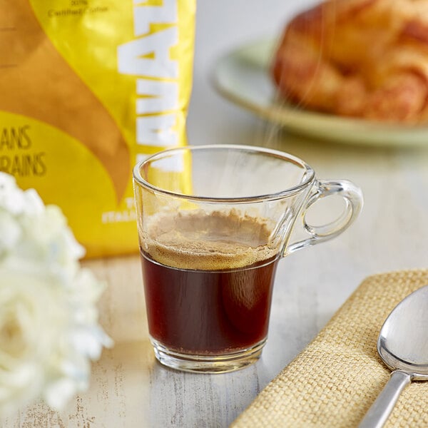 A cup of Lavazza coffee with a bag of Lavazza Tierra! Colombia Whole Bean Espresso on a table.