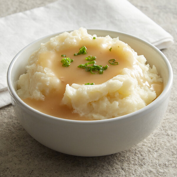 A bowl of mashed potatoes topped with gravy and chopped chives.