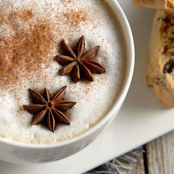 A cup of coffee with star anise and cinnamon next to a blurry pastry.