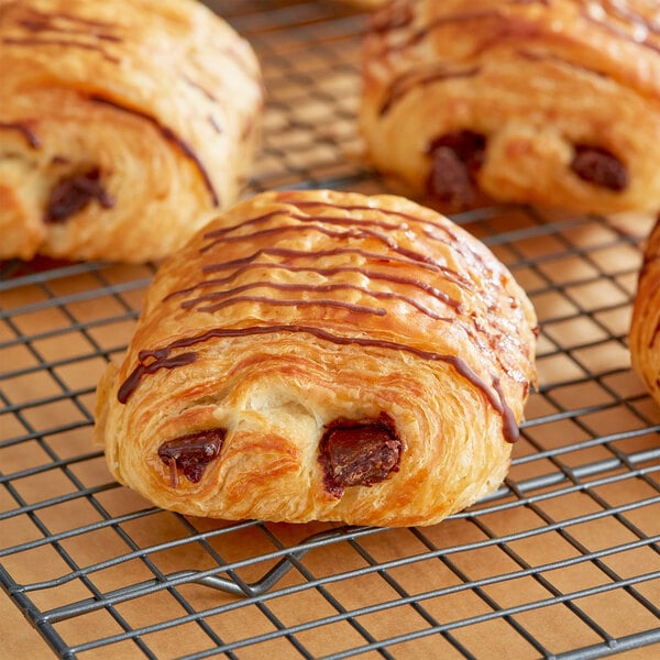 A cooling rack with chocolate croissants on it.