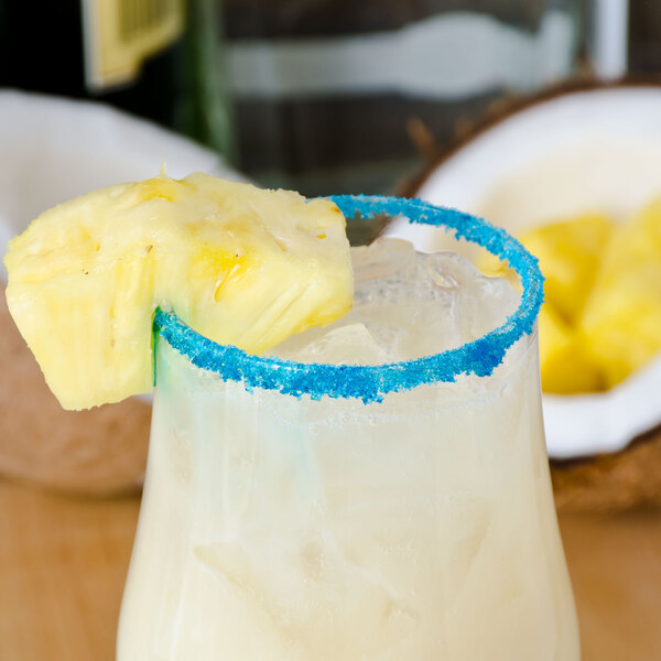 A glass with a drink rimmed with Rokz Pina Colada cocktail sugar and garnished with a pineapple slice.