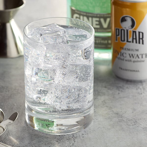 A glass of water with ice and a can of Polar tonic water on a table.