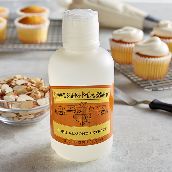 A white bottle of Nielsen-Massey almond extract next to a cupcake.