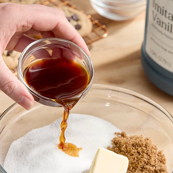 A person pouring Hometown Provisions imitation vanilla into a bowl of brown liquid.