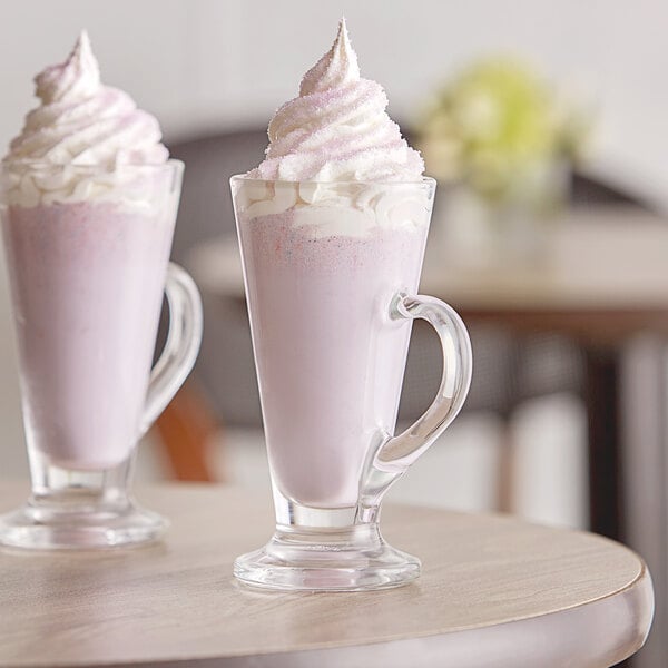 A glass of Capora Taro frappe mix with pink liquid and whipped cream on top.