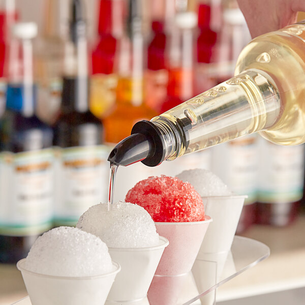A person pouring Hawaiian Shaved Ice Coconut Snow Cone Syrup over snow cones.