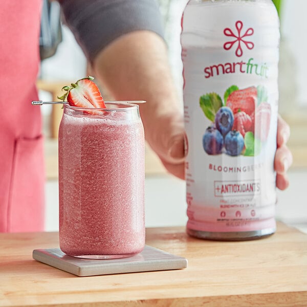 A person holding a bottle of Smartfruit Blooming Berry smoothie mix.