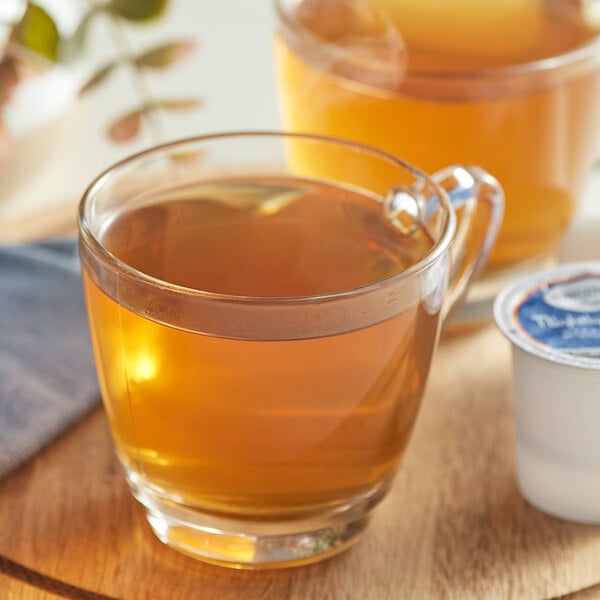 A glass cup of Twinings Nightly Calm herbal tea on a wooden tray.