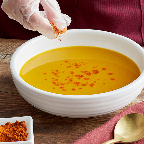 A person adding Regal Mild Ground Cayenne Pepper to a bowl of soup.