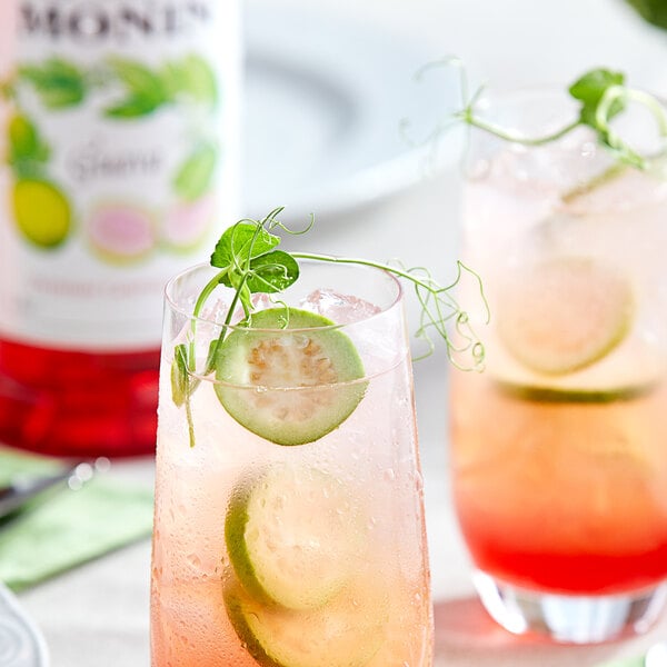 A glass of pink Monin guava drink with cucumber slices and mint on a table.