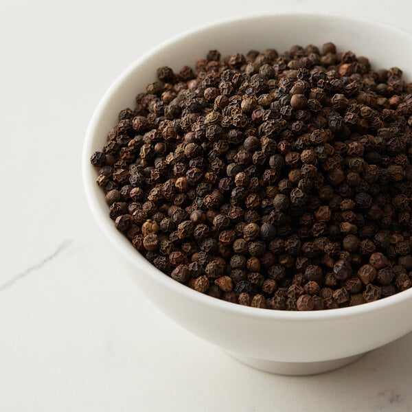 A bowl of Regal Whole Black Peppercorns on a white surface.