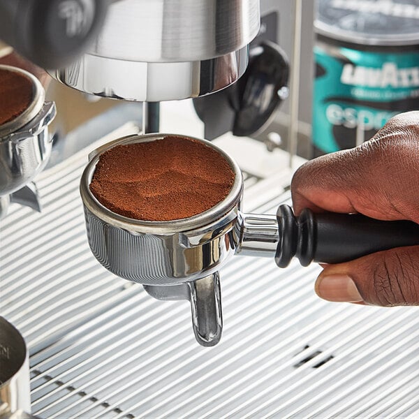 A hand using a black Lavazza coffee machine to make espresso with Lavazza Decaf Espresso powder.