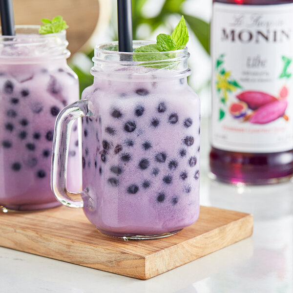 Two glasses of purple Monin Ube drinks with mint leaves and black straws.