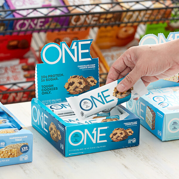A person holding a package of ONE 12-Count Chocolate Chip Cookie Dough Protein Bars.
