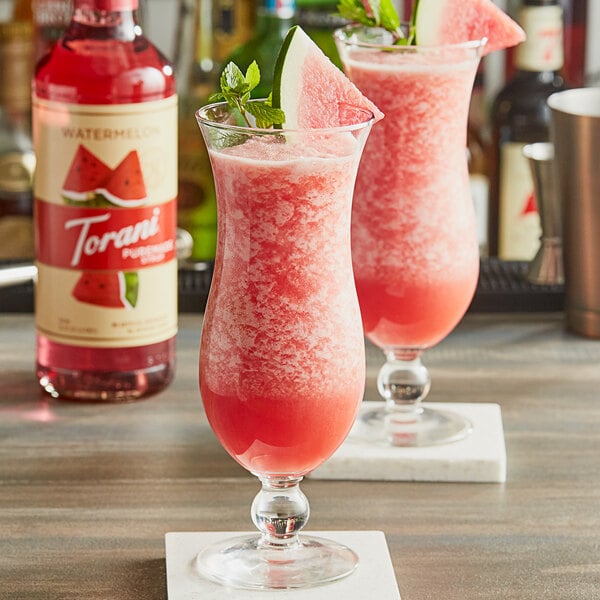 Two glasses of watermelon and mint cocktails made with Torani Watermelon Flavoring Syrup on a table.