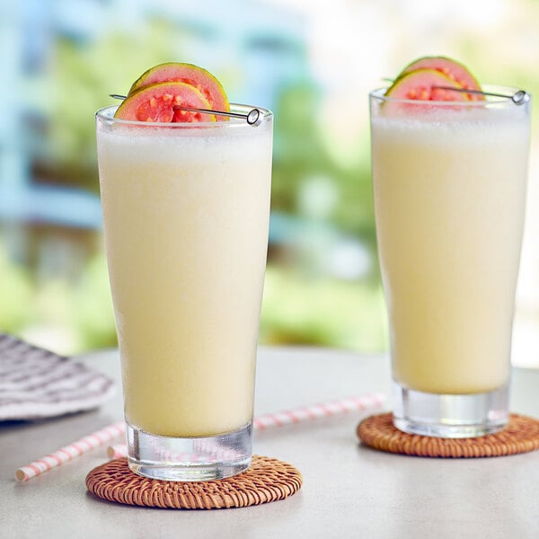 Two glasses of Capora Guava Passion Fruit smoothies with fruit on top.