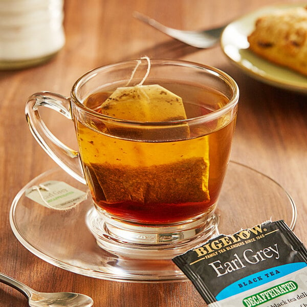 A glass cup of Bigelow Earl Grey Decaffeinated Tea with a tea bag on a saucer.