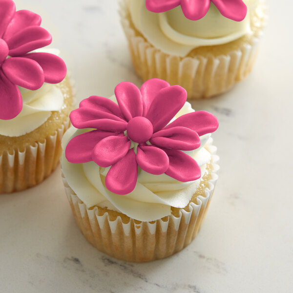 Three cupcakes with Satin Ice ChocoPan pink flower decorations on top.