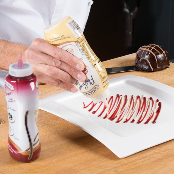 A hand pouring Smucker's vanilla sauce from a plastic bottle onto a chocolate dessert.