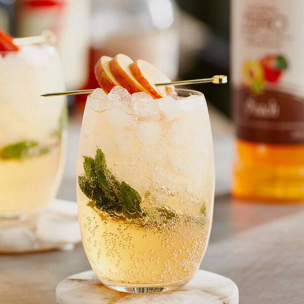 Two glasses of peach drinks with ice and mint leaves, garnished with sliced peaches.