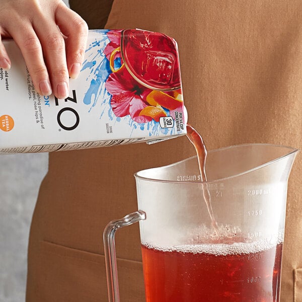 A hand pouring Tazo Sweetened Passion Iced Herbal Tea into a pitcher.