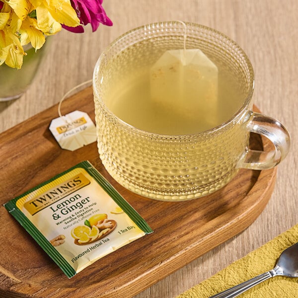 A cup of Twinings Lemon & Ginger tea with a bag on a tray.