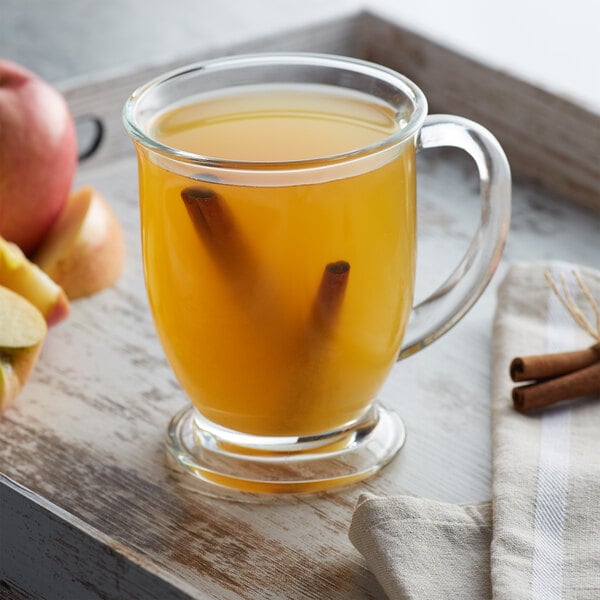 A glass mug of apple cider with cinnamon sticks on the side.