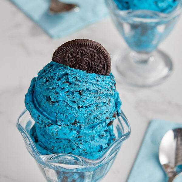 A glass bowl of blue ice cream with an Oreo cookie on top.