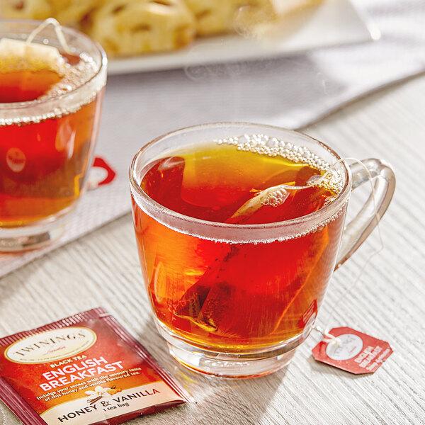 A glass cup of Twinings English Breakfast tea with a tea bag next to a plate of pastries.