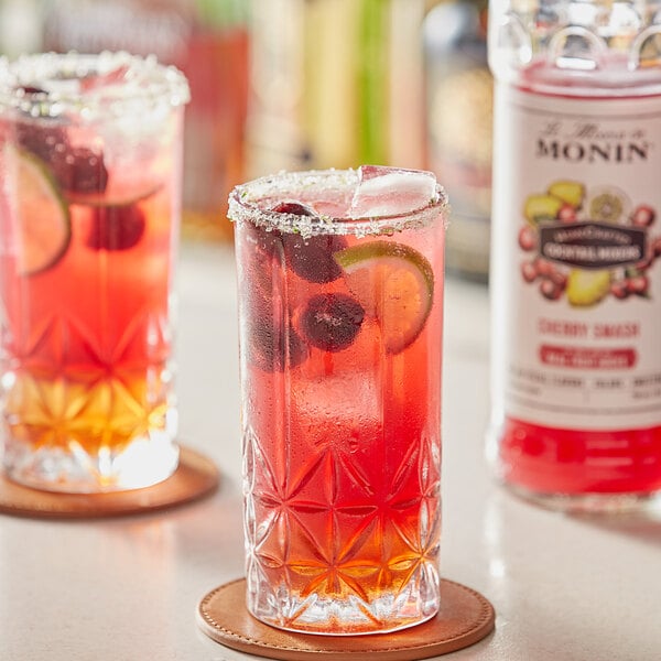A glass of Monin Cherry Smash cocktail with fruit garnish on a table.