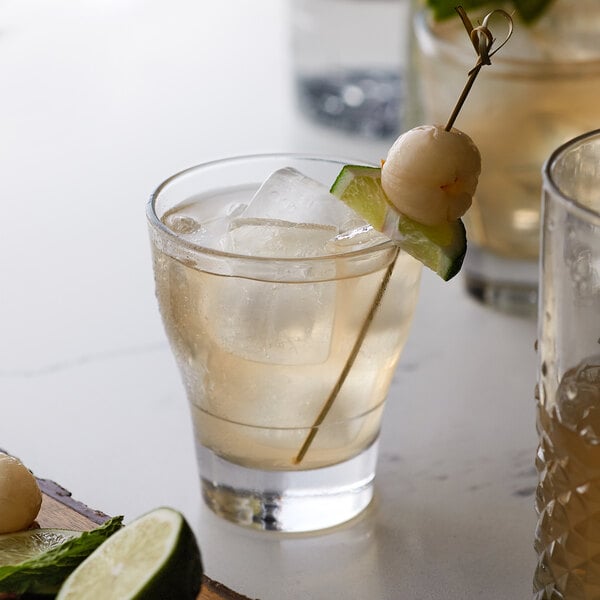 A glass with liquid and ice, a stick, and a lime on a table.