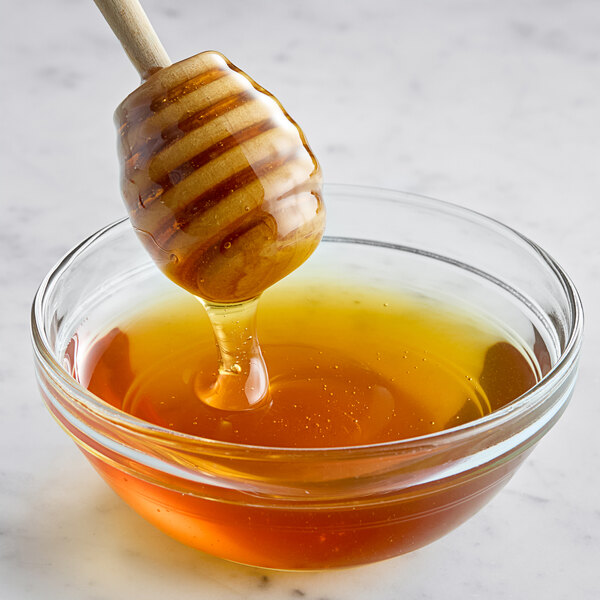 A honey dipper dripping Hometown Provisions Alfalfa Honey into a bowl.