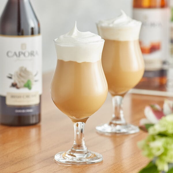 A bottle of Capora Irish Cream flavoring syrup with two glasses of liquid and whipped cream.