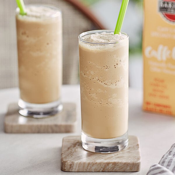 Two glasses with a brown Barista Fria Caffe Latte drink on a table.