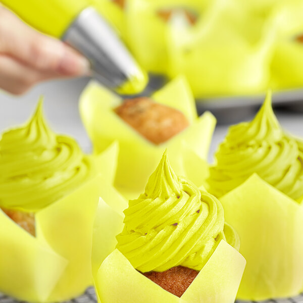 A close-up of a pastry brush adding Chefmaster Neon Brite Yellow food coloring to yellow frosted cupcakes.